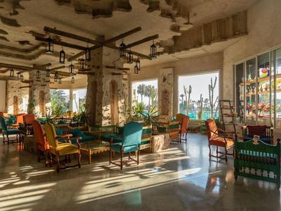 Lounge dell'hotel luminosa con sedute colorate e grandi finestre con vista sulle palme.