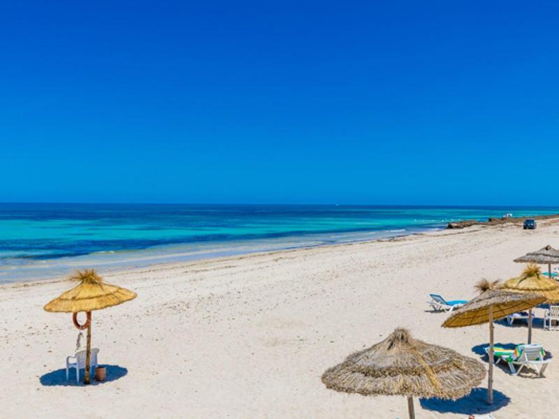 Spiaggia di sabbia bianca con ombrelloni di paglia e acqua limpida sotto un cielo azzurro.