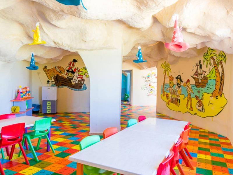 Area giochi per bambini con pavimento colorato, tavoli e sedie in design a parete di grotta.