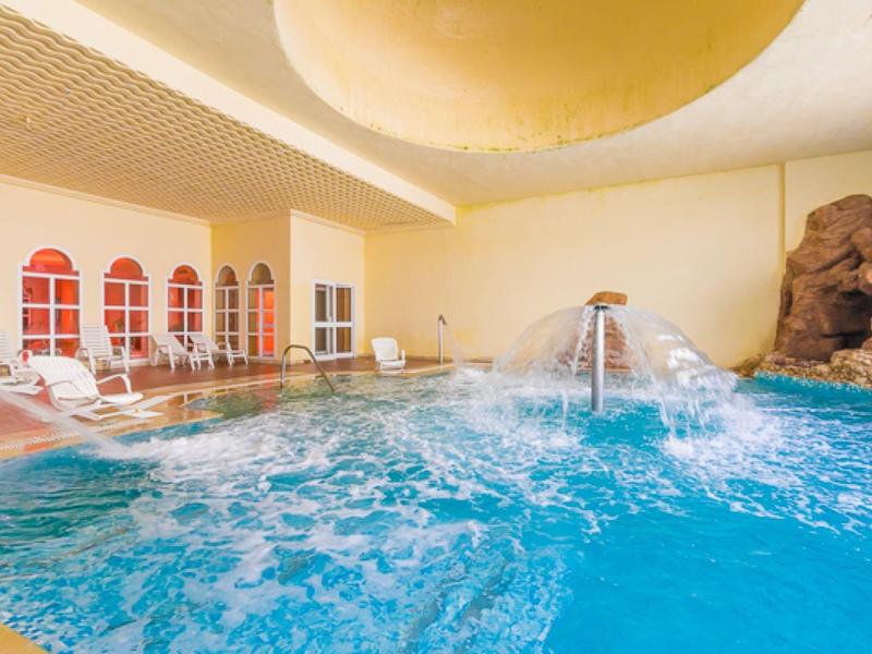 Piscina interna con cascata e lettini in area benessere luminosa dell'hotel.