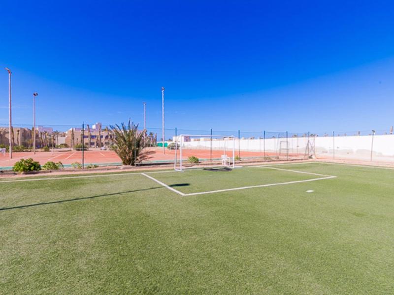 Struttura sportiva all'aperto con prato sintetico e campi da tennis sotto un cielo azzurro.