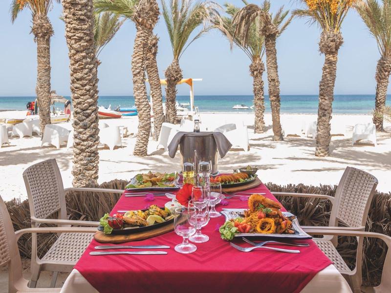 Tavolo apparecchiato con cibo e palme con spiaggia sullo sfondo