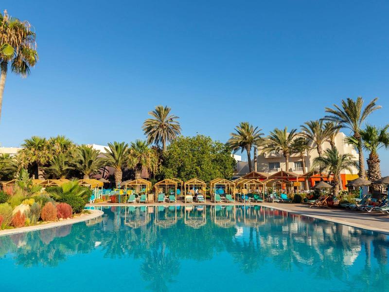 Una grande piscina all'aperto con lettini, palme e cielo azzurro in un resort alberghiero.