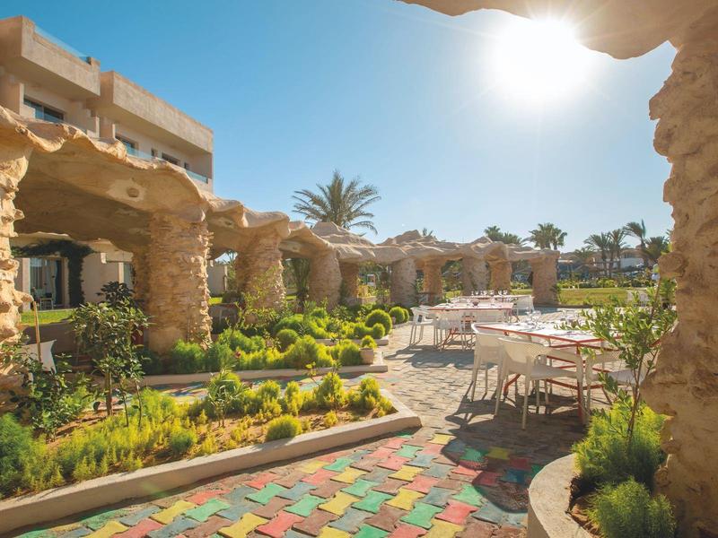 Terrazza giardino soleggiata con tavoli, sedie e archi in pietra in un hotel.