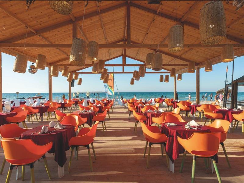 Ristorante all'aperto con sedie rosse e vista sul mare in una giornata di sole