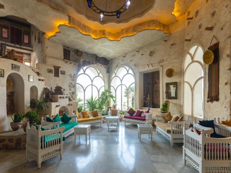 Lounge dell'hotel luminosa con grandi finestre, mobili bianchi e cuscini colorati