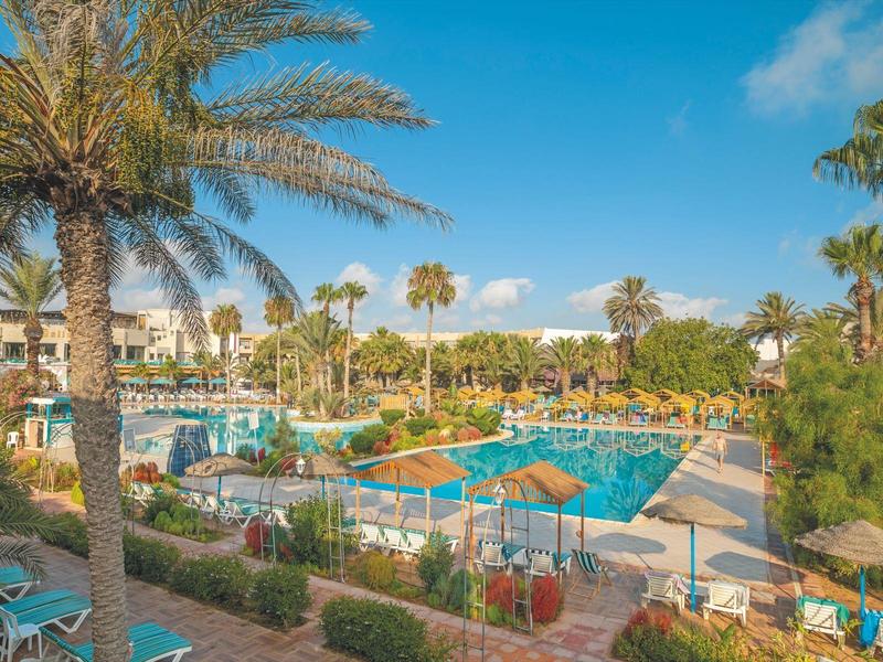 Piscina dell'hotel con lettini e palme sotto un cielo azzurro.