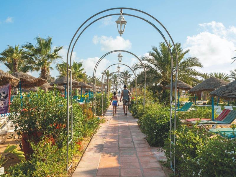 Un sentiero con lampade, fiancheggiato da palme e ombrelloni, attraversa una località tropicale.