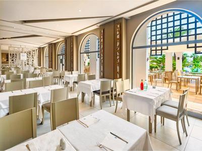 Helles, modernes Restaurant mit weißen Tischen, grauen Stühlen und großen bogenförmigen Fenstern.