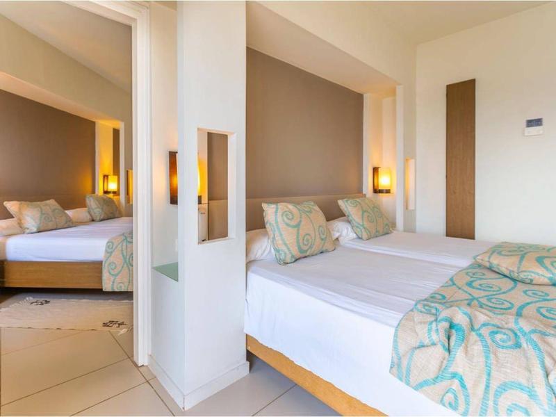 Helles, modernes Schlafzimmer mit zwei Einzelbetten, beigen Wänden und verzierten Bettdecken.