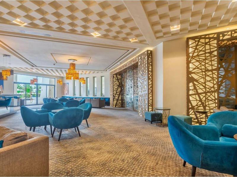 Großer, moderner Raum mit blauen Sesseln, Teppichboden, großen Fenstern und dekorativen Wandelementen.