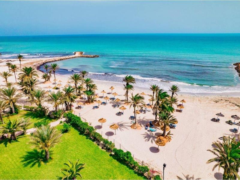 Strand mit weißem Sand, Palmen, Sonnenschirmen und türkisblauem Meer.