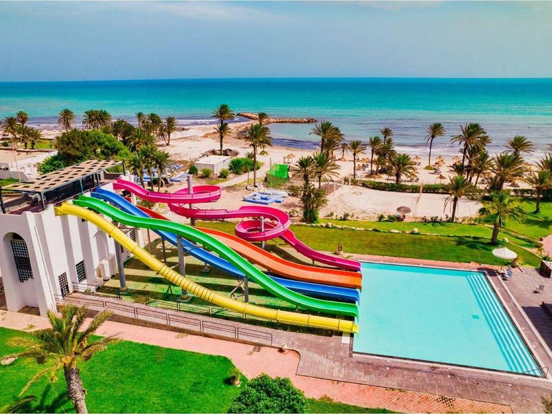 Wasserpark mit bunten Rutschen, Pool, Palmen und einem Sandstrand im Hintergrund am Meer.