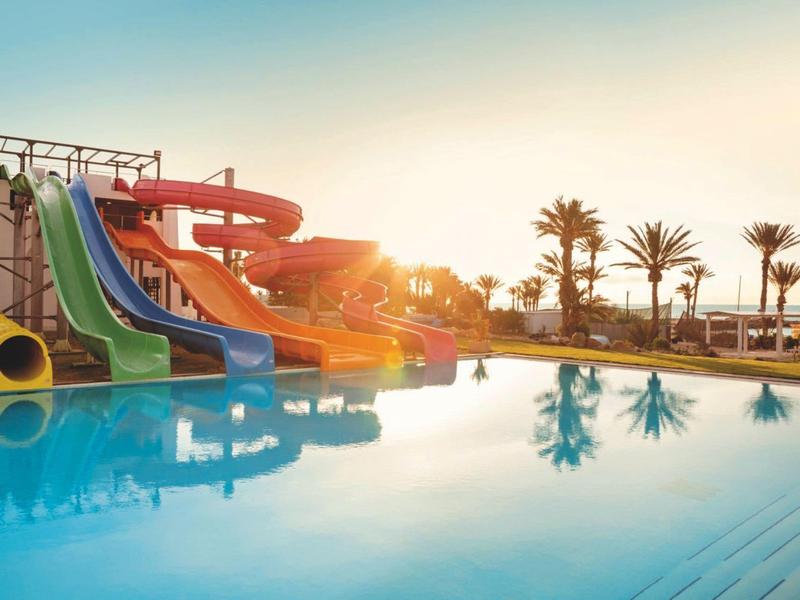 Bunter Wasserrutschenpark mit großem Pool und Palmen im Sonnenuntergang am Strand.