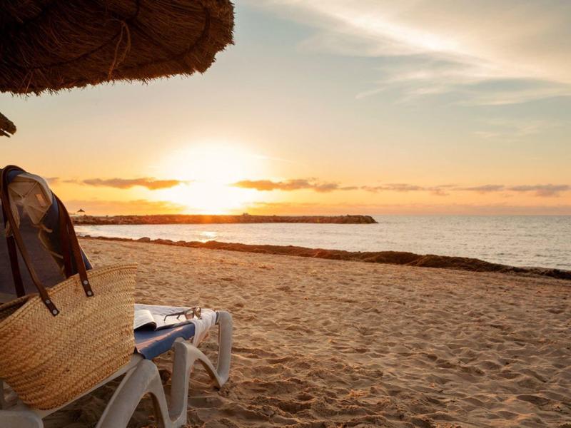 Sonnenuntergang am Strand mit Liegestühlen und Strohdach im Vordergrund.