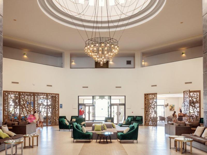 Großer runder Raum mit beleuchtetem Kronleuchter, grünen Sesseln, Sofas und dekorativen Elementen.