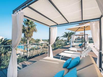 Luxuriöse Terrasse mit weißen Loungemöbeln, blauen Kissen und Palmen vor klarem Himmel.