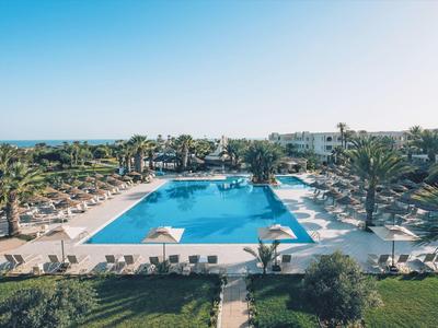 Grande piscina dell'hotel con lettini e palme sotto cielo limpido.