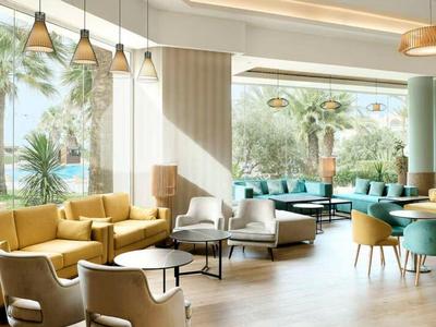 Helles Hotel-Lounge mit bequemen Sitzgelegenheiten, großen Fenstern und Blick auf Palmen.