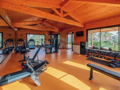 Fitnessraum mit Holzdecken, großen Fenstern und moderner Trainingsausrüstung.