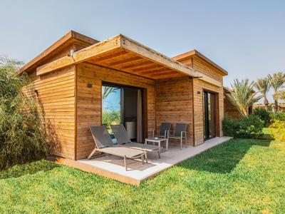 Casa vacanze moderna in legno con terrazza, sdraio e giardino curato sotto un cielo limpido.