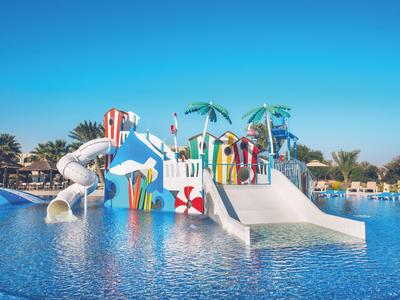 Wasserpark mit bunten Rutschen, Palmen und klares blaues Wasser unter strahlend blauem Himmel.