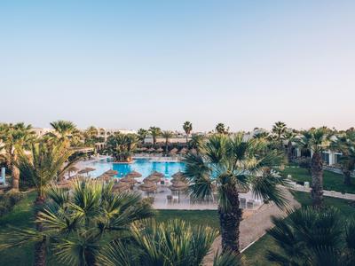 Großer Pool mit Palmen und Sonnenschirmen in einem tropischen Resort bei klarem Himmel.