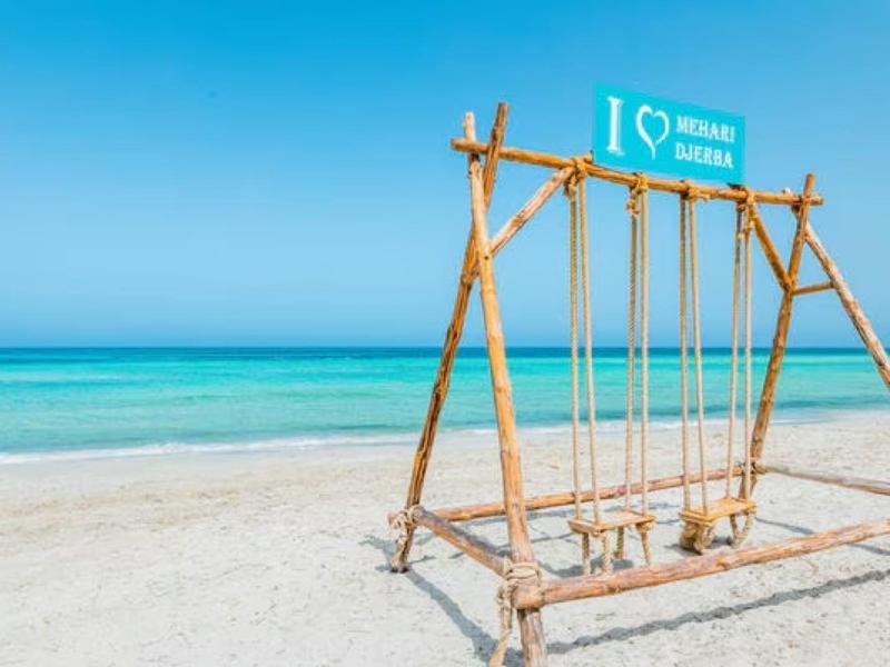 Altalena di legno sulla spiaggia di sabbia bianca con mare e cielo blu chiaro sullo sfondo