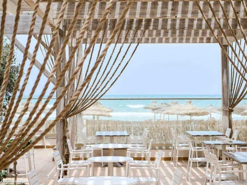 Ristorante sulla spiaggia aperto con tavoli bianchi e vista sul mare.
