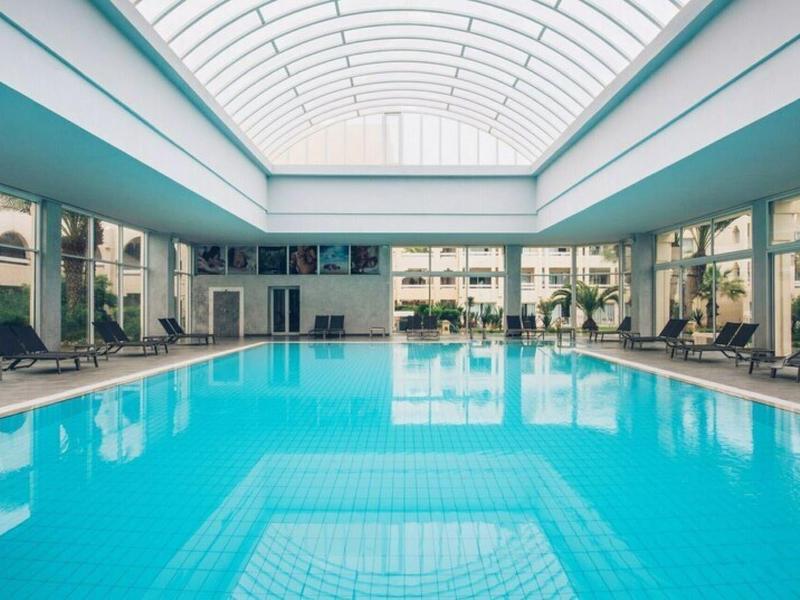 Grande piscina coperta con lettini sotto un tetto di vetro in un hotel.