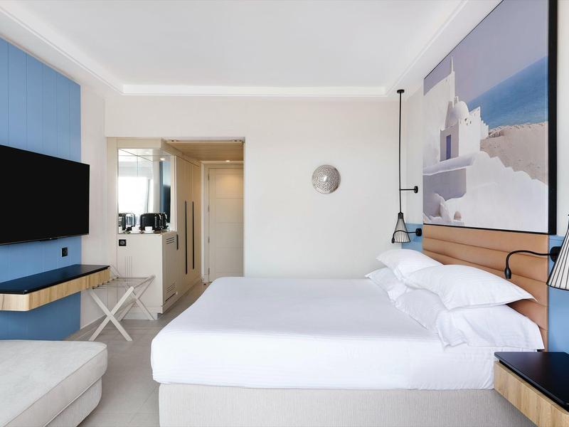 Camera d'hotel luminosa con letto matrimoniale, quadro a parete, TV e arredamento moderno.