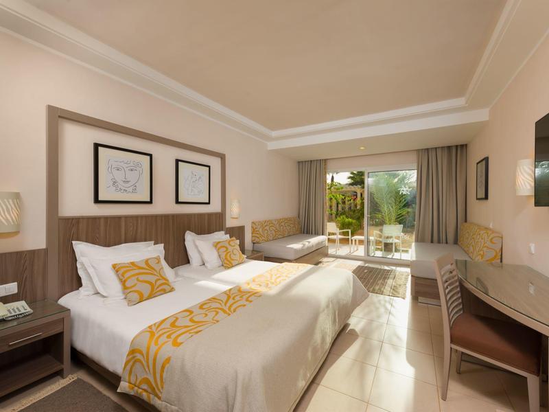 Camera d'hotel luminosa con letto matrimoniale, letto singolo e balcone con terrazza.