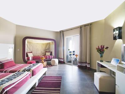 Modernes Hotelzimmer mit zwei Betten, großem Spiegel, TV, Sitzbereich und Balkonzugang.