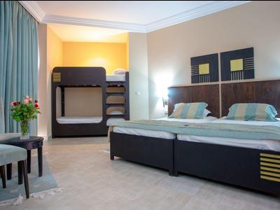 Ein gemütliches Hotelzimmer mit zwei Einzelbetten, Etagenbett, Stühlen und Blumen auf dem Tisch.