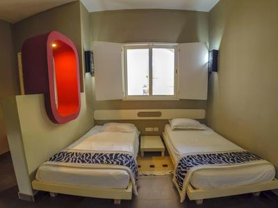 Zweibettzimmer mit zwei Einzelbetten, grauen Wänden und roter Nische an der Wand.