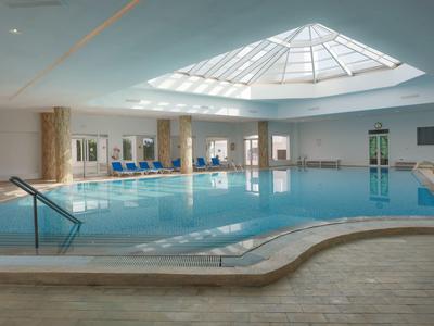 Grande piscina coperta luminosa con tetto in vetro e comodi posti a sedere lungo il bordo.