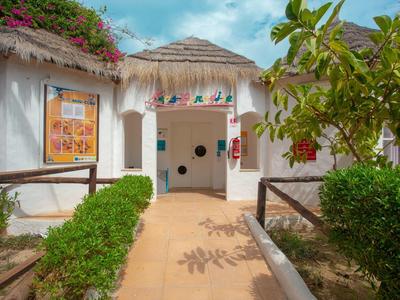 Ingresso di un edificio alberghiero tropicale bianco con tetto di paglia e piante verdi.