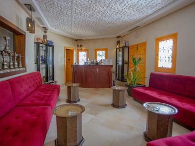 Area lounge di hotel luminosa con poltrone rosse e piccoli tavoli rotondi.