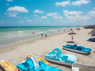 Strand mit blauer Liege und Sonnenschirmen, Menschen genießen einen sonnigen Tag am Meer.