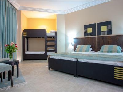 Camera d'hotel moderna con letto matrimoniale, letto a castello, sedie e vista sulle tende.