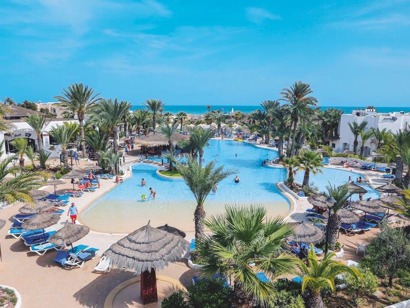 Grande piscina dell'hotel con palme e lettini, vista sul mare sotto un cielo blu