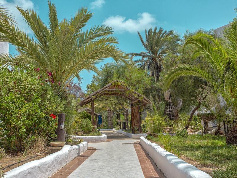 Un sentiero lastricato attraversa un giardino tropicale con palme fino a un padiglione in legno.