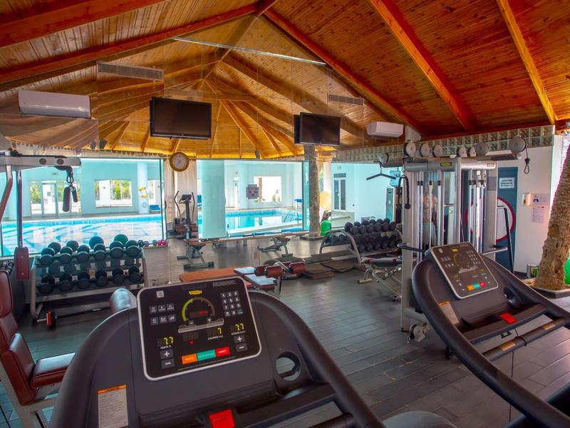 Vista interna di una palestra con tapis roulant e rastrelliere per manubri sotto travi di legno.