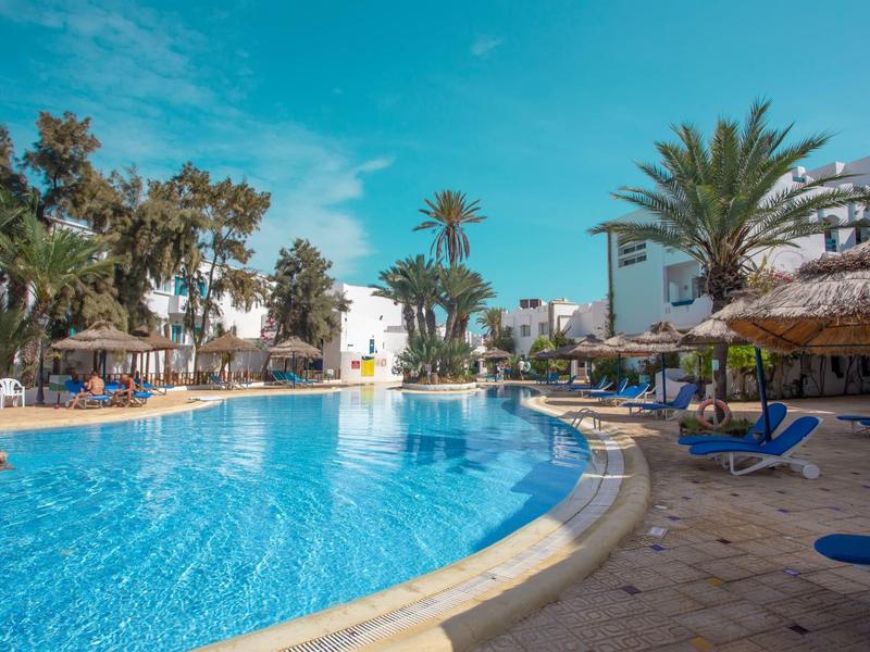 Grande piscina con lettini e palme in un complesso alberghiero in una giornata di sole.