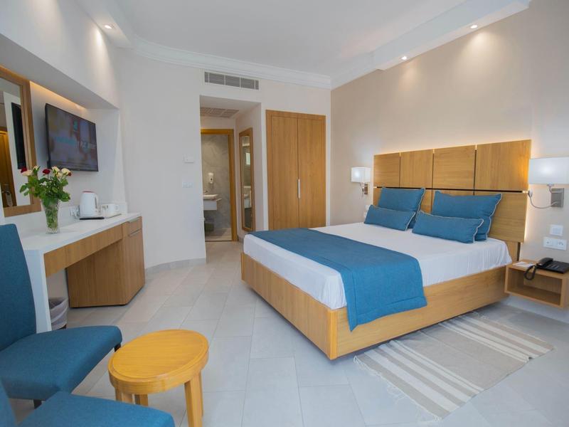 Camera d'hotel moderna con letto matrimoniale, decorazione blu e zona salotto con sedia e tavolo