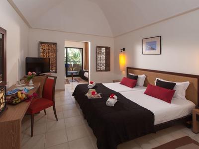 Modern eingerichtetes Hotelzimmer mit zwei großen Betten, Schreibtisch, Stühlen und Zugang zu Balkon.