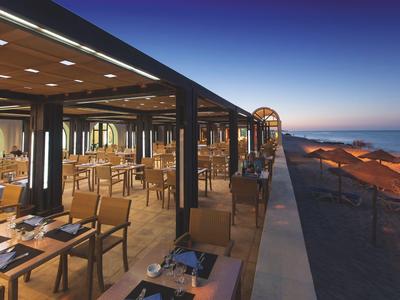 Offenes Restaurant mit Holztischen und Blick auf den Sonnenuntergang am Strand.