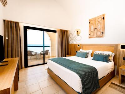 Modernes Hotelzimmer mit Doppelbett, Holzmöbeln und Blick auf das Meer durch eine Glas-Schiebetür.