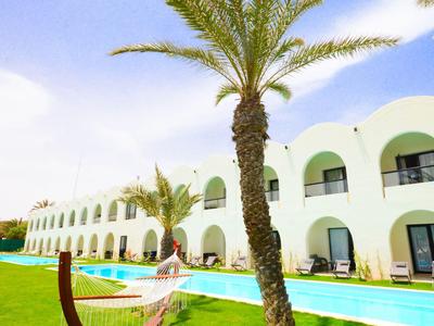 Hotelanlage mit weißem Gebäude, Schwimmbad, Palmen und einer Hängematte auf dem Rasen.