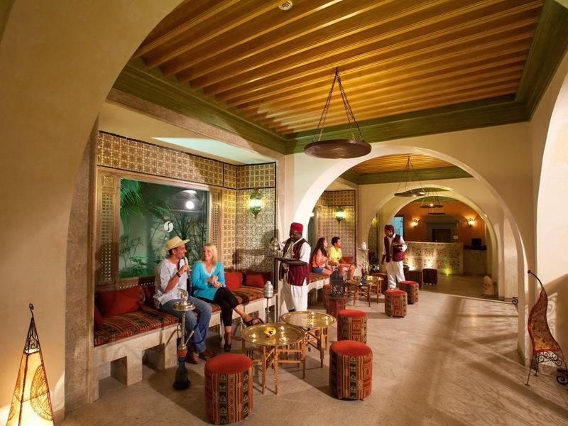 Accogliente lounge dell'hotel con panche, sedie e illuminazione soffusa dai toni caldi.